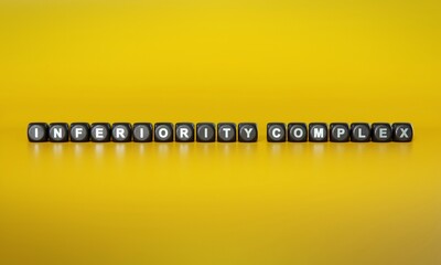 Term ‘Inferiority complex’ spelled out in white text on dark wooden blocks against plain yellow background. 3D rendering
