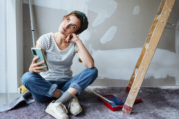 Young woman with cell phone thinking how to renovate her apartment - 509795270