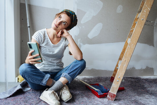 Young woman with cell phone thinking how to renovate her apartment