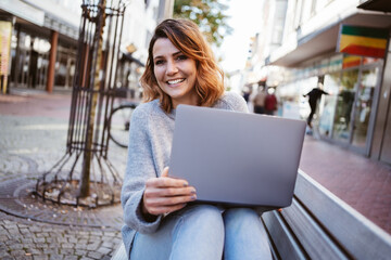Fototapeta na wymiar Woman sitting on park bench with laptop and smiling at camera