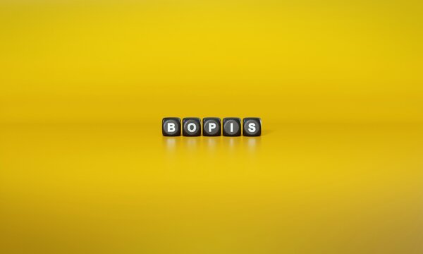 Acronym &lsquo;BOPIS&rsquo; spelled out in white text on dark wooden blocks against plain yellow background. 3D rendering