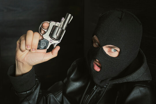 a masked bandit hides in the dark with a firearm. Threat to life. Close-up of hand with pistol. Shootout of criminals with revolvers. Dark background and dangerous situation. Killer or murderer.