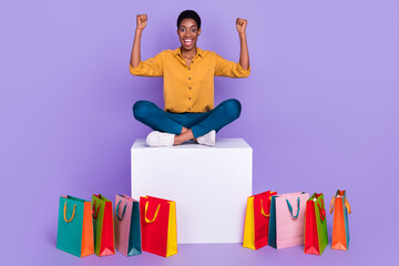 Portrait of beautiful trendy cheery lucky girl sitting on box rejoicing having fun black friday gifts isolated on violet purple color background