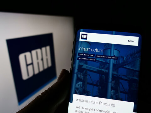 Stuttgart, Germany - 05-29-2022: Person holding smartphone with webpage of Irish building materials company CRH plc on screen in front of logo. Focus on center of phone display.