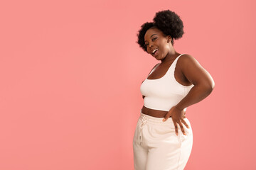 Studio shot of happy dark skinned, young woman with afro hairstyle, smiling and posing over pink...