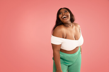 Joyful Plus Size african Woman laughing, posing on a pastel pink Studio Background. Real people...