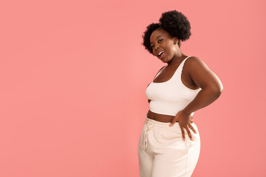 Studio shot of happy dark skinned, young woman with afro hairstyle, smiling and posing over pink pastel studio background.