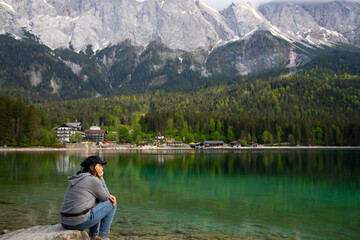 Caucasian female sitting on a stone near the Eibsee Lake, Germany. Travel, lifestyle concept.
