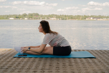 a young girl is doing yoga on the shore on the yoga mat of the river in the evening