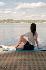 Fototapeta na wymiar a young girl is doing yoga on the shore on the yoga mat of the river in the evening