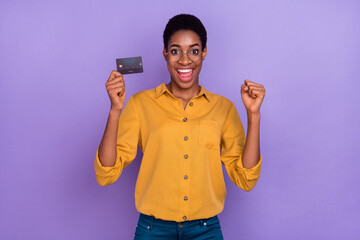Portrait of attractive brunet cheery trendy skilled girl holding atm card rejoicing isolated over...