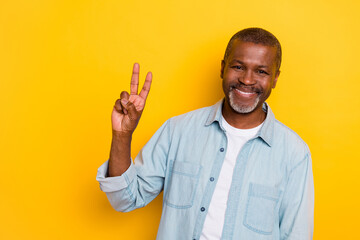 Portrait of satisfied person hand fingers demonstrate v-sign symbol toothy smile isolated on yellow...