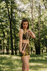 a young girl goes in for sports with elastic for fitness in the park / in the forest. in a green suit on a yoga mat