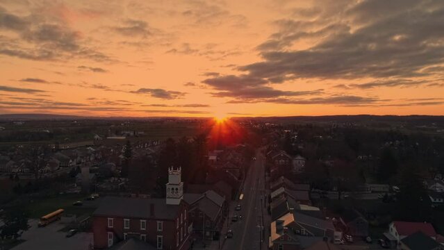 A Drone Approaching View of a Small Town and a Steeple at Sunrise as it gets Ready to Break the Horizon, with Orange and Reds on a Spring Sunrise With Partial Cloudy Skies.