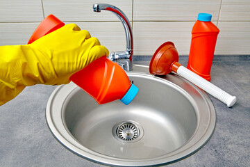 Hands in yellow rubber gloves hold a plunger and a pipe cleaner against the background of a kitchen...