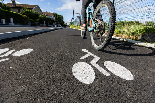 Piste cyclable avec un cycliste le long d'une route, la piste est séparée par un trottoir, le sol possède un marquage blanc pour indiquer le sens des vélos