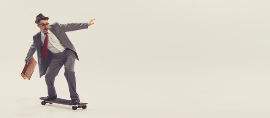 Young funny man, businessman dressed in suit in 50s, 60s fashion style rides skateboard isolated on...