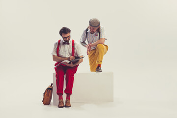 Two cheerfull dudes, young men in old-school fashioned attire reading magazine isolated on white...