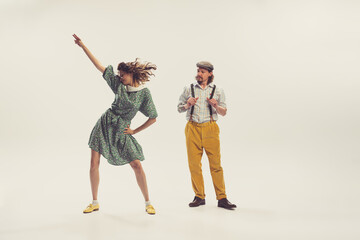 Young man and woman in vintage retro style outfits dancing social dance isolated on white background. Timeless traditions, 1960s american fashion style and art.