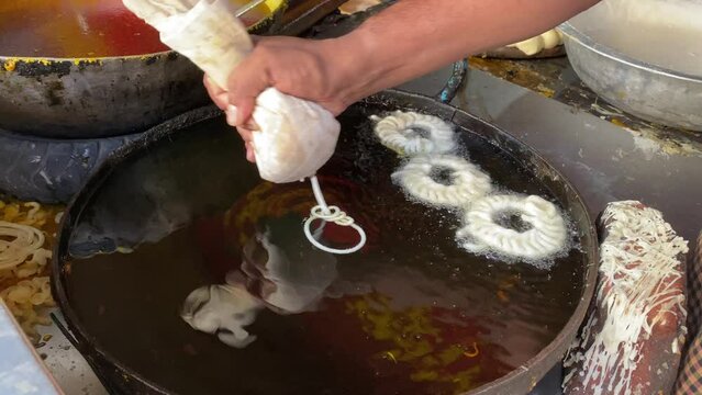 Man making traditional sweet orange jalebi snacks on a street food market at Sharma snacks in Kolkata, India.