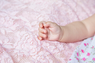 closeup hand of a baby girl lying on pink lace blanket 