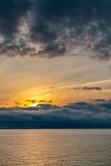 Dramatic storm clouds above sea water surface with golden sunrise behind the clouds on a warm day of early autumn.