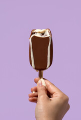 Melting ice cream on stick in milk chocolate glaze in hand on  purple background