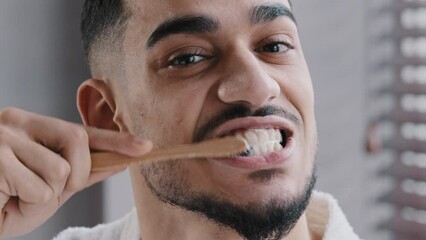 Extreme close up head shot bearded adult handsome Indian Spaniard Arab man brushing teeth in bathroom. Portrait hipster Arabic ethnicity guy doing oral mouth hygienic daily toothy procedure, toothcare