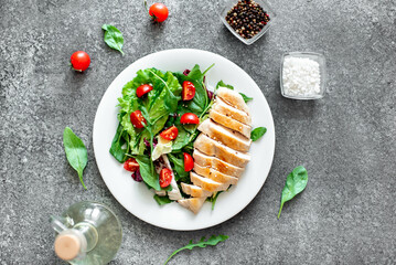 Grilled chicken breast and salad with tomato, spinach, asberg, radichio, arugula on a stone background