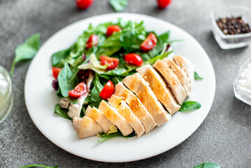 Grilled chicken breast and salad with tomato, spinach, asberg, radichio, arugula on a stone background