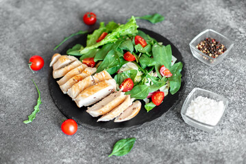 Grilled chicken breast and salad with tomato, spinach, asberg, radichio, arugula on a stone background