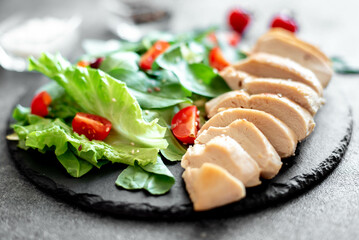 Grilled chicken breast and salad with tomato, spinach, asberg, radichio, arugula on a stone background