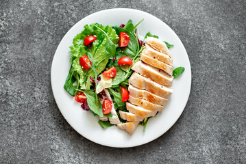 Grilled chicken breast and salad with tomato, spinach, asberg, radichio, arugula on a stone background
