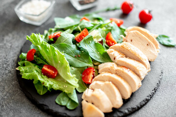 Grilled chicken breast and salad with tomato, spinach, asberg, radichio, arugula on a stone background