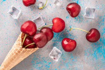 ripe and fresh cherries and ice cubes popping out of ice cream waffle cone on blue gray background