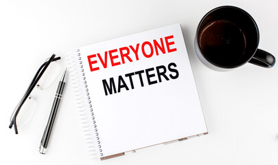 Coffee,glasses,pen and notebook written with EVERYONE MATTERS , on white background.