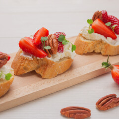 Freshly prepared vegetarian sandwiches with cream cheese, strawberry sliced, pecans, arugula on wooden board. Healthy toast for breakfast or lunch.  Selective focus.