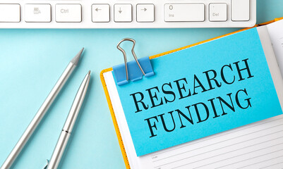 RESEARCH FUNDING text on sticker on the blue background with pen and keyboard