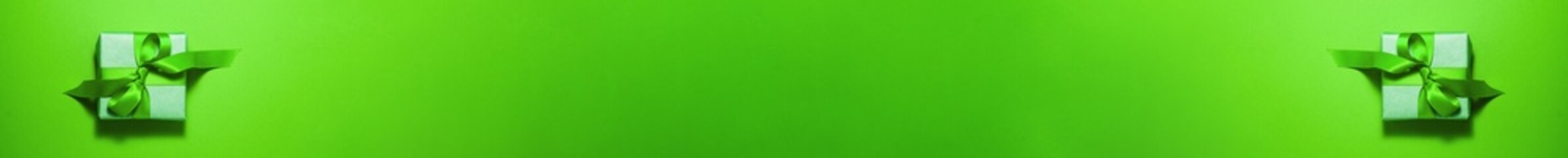 Banner of brown paper gift box with a green satin ribbon bow on top on green background. Christmas holiday mother and father Valentines days and birthday present flat lay concept with copy space.