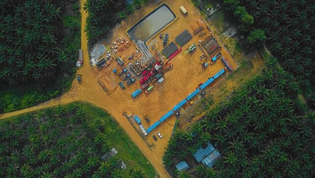 Cinematic Onshore Drilling and Workover Rig structure and Rig equipment for oil exploration and exploitation in the middle of jungle surrounded by palm oil trees during sunset time.