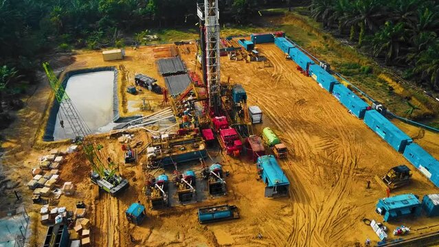 Cinematic Onshore Drilling and Workover Rig structure and Rig equipment for oil exploration and exploitation in the middle of jungle surrounded by palm oil trees during sunset time.