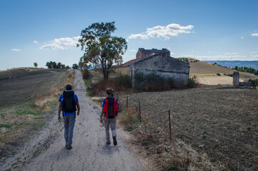 Pellegrini in cammino lungo la Via Peuceta del Cammino Materano passano davanti ad una casa...