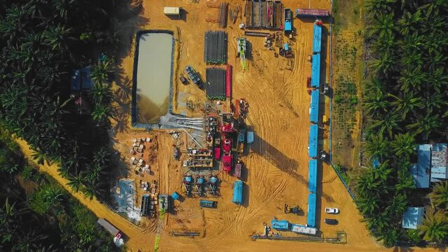 Cinematic Onshore Drilling and Workover Rig structure and Rig equipment for oil exploration and exploitation in the middle of jungle surrounded by palm oil trees during sunset time.