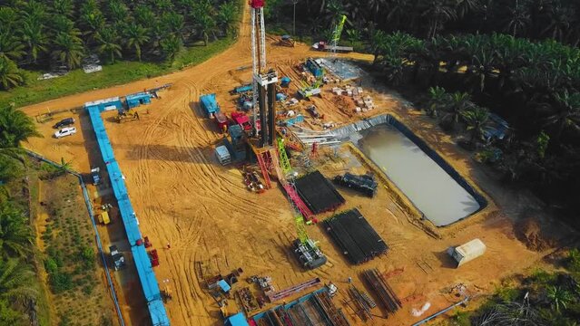 Cinematic Onshore Drilling and Workover Rig structure and Rig equipment for oil exploration and exploitation in the middle of jungle surrounded by palm oil trees during sunset time.
