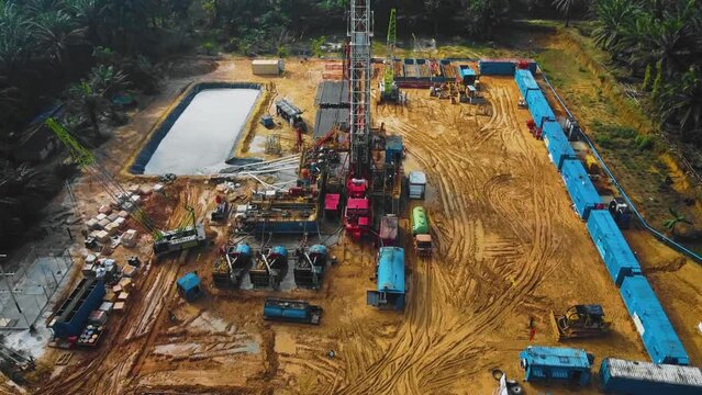 Cinematic Onshore Drilling and Workover Rig structure and Rig equipment for oil exploration and exploitation in the middle of jungle surrounded by palm oil trees during sunset time.