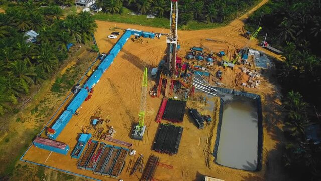 Cinematic Onshore Drilling and Workover Rig structure and Rig equipment for oil exploration and exploitation in the middle of jungle surrounded by palm oil trees during sunset time.