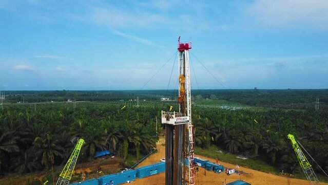 Cinematic Onshore Drilling and Workover Rig structure for oil exploration and exploitation in the middle of jungle surrounded by palm oil trees during sunset time.