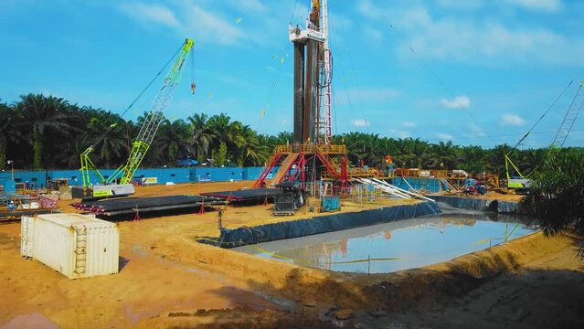 Cinematic Onshore Drilling and Workover Rig structure and Rig equipment for oil exploration and exploitation in the middle of jungle surrounded by palm oil trees during sunset time.