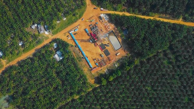 Cinematic Onshore Drilling and Workover Rig structure and Rig equipment for oil exploration and exploitation in the middle of jungle surrounded by palm oil trees during sunset time.