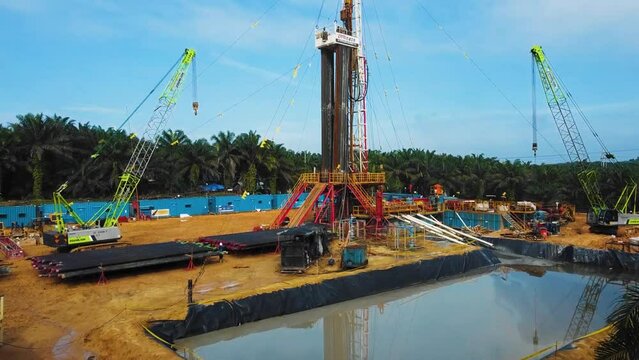 Cinematic Onshore Drilling and Workover Rig structure for oil exploration and exploitation in the middle of jungle surrounded by palm oil trees during sunset time.